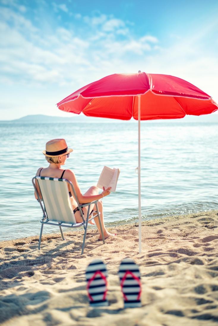 vrouw leest boek op strand met parasol